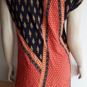 May include: Black and red patterned top with gold accents. The top has a scoop neck and short sleeves.