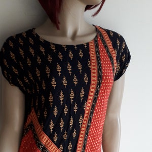 May include: A black and red short-sleeved dress with a gold and black floral print. The dress has a diagonal pattern with a red and gold trim.