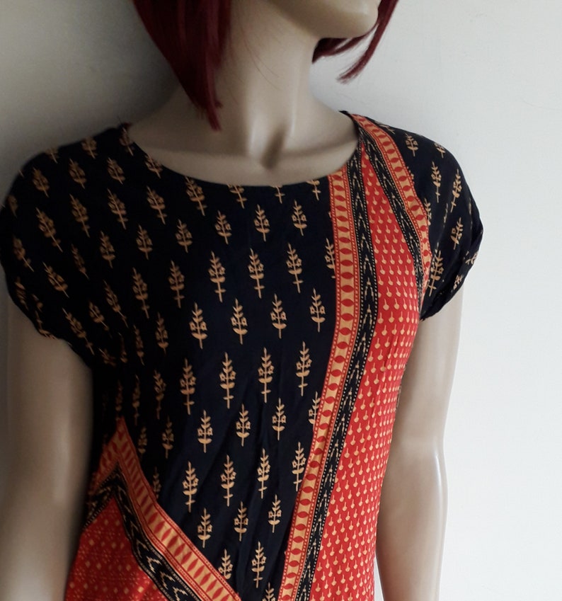 May include: A black and red short-sleeved dress with a gold and black floral print. The dress has a diagonal pattern with a red and gold trim.