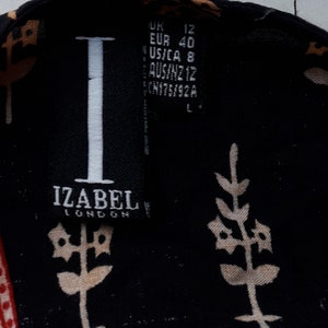 May include: A black and white label with the text "IZABEL LONDON" and size information in inches, centimeters, and other international sizing systems. The label is attached to a black fabric with a white floral pattern.