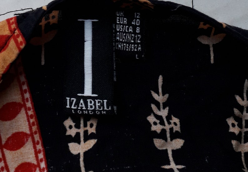 May include: A black and white label with the text "IZABEL LONDON" and size information in inches, centimeters, and other international sizing systems. The label is attached to a black fabric with a white floral pattern.