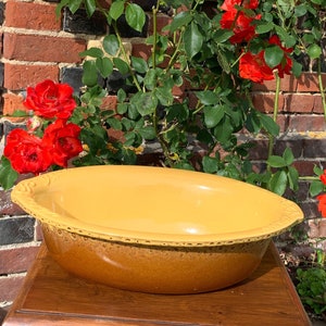 May include: A large, oval-shaped, yellow ceramic baking dish with a brown glaze. The dish has a slightly raised rim and a textured surface. The dish is sitting on a wooden table.