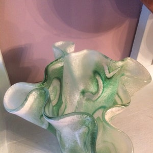 May include: A green and white glass vase with a ruffled, wavy design. The vase has a translucent, frosted look with swirls of green and white.