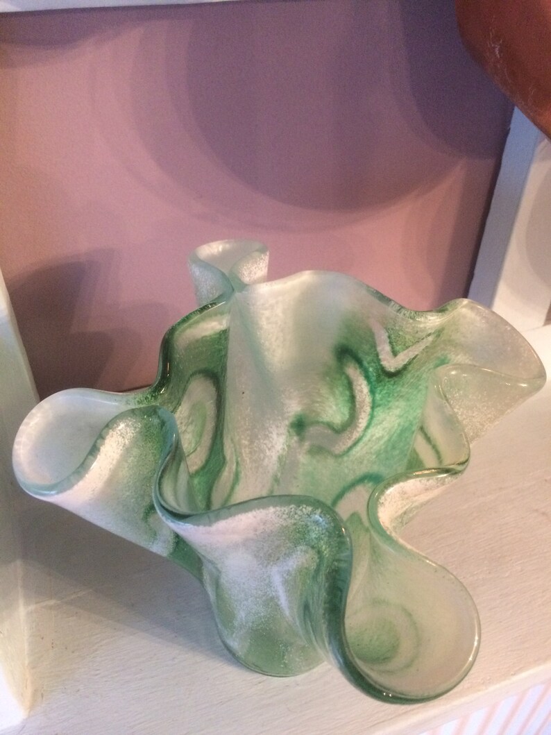 May include: A green and white glass vase with a ruffled, wavy design. The vase has a translucent, frosted look with swirls of green and white.