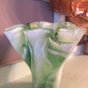 May include: A green and white glass vase with a wavy, ruffled design. The vase has a speckled, textured surface.