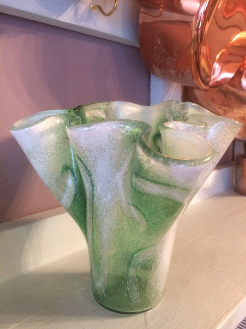 May include: A green and white glass vase with a wavy, ruffled design. The vase has a speckled, textured surface.