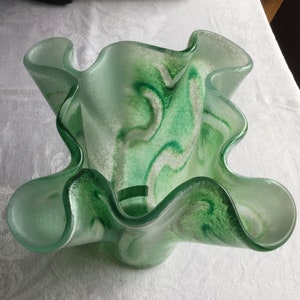 May include: A green glass vase with a wavy, ruffled design. The vase has a white and green marbled pattern.