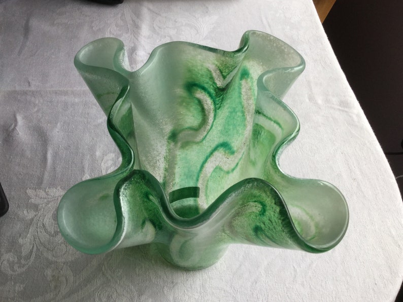May include: A green glass vase with a wavy, ruffled design. The vase has a white and green marbled pattern.
