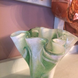 May include: A green and white glass vase with a ruffled, organic shape. The vase has a swirl pattern and a speckled texture.