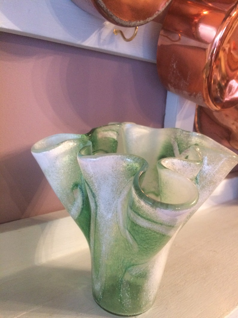 May include: A green and white glass vase with a ruffled, organic shape. The vase has a swirl pattern and a speckled texture.