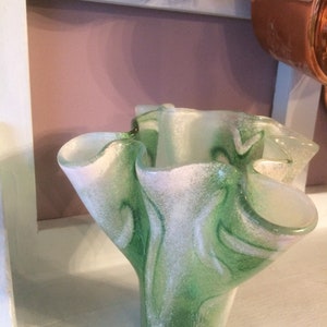 May include: A green and white glass vase with a ruffled, organic shape. The vase has a speckled, textured surface.