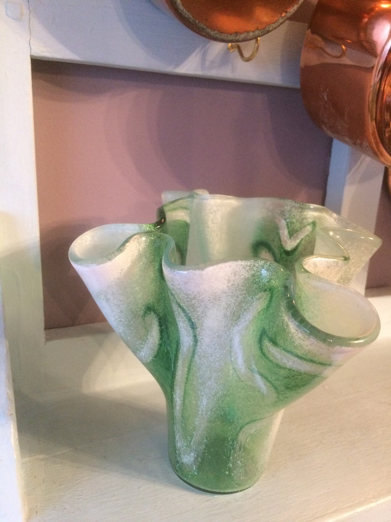 May include: A green and white glass vase with a ruffled, organic shape. The vase has a speckled, textured surface.