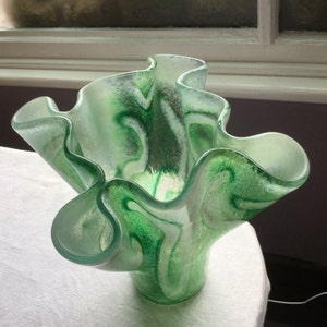 May include: A green and white glass vase with a ruffled, wavy design. The vase is made of clear glass with green and white swirls.