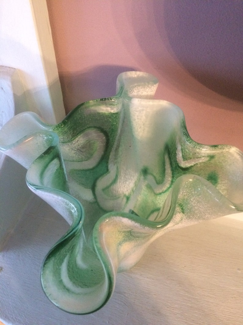 May include: A green and white glass vase with a wavy, ruffled design. The vase has a textured, frosted finish.