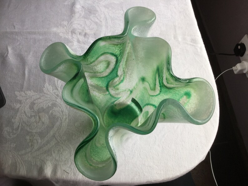 May include: A green glass bowl with white swirls. The bowl has a wavy, organic shape.
