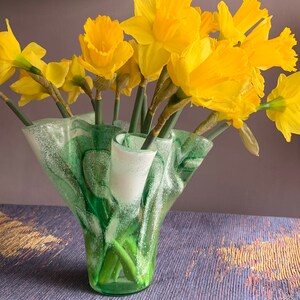 May include: A green glass vase with a ruffled, textured design holds a bouquet of yellow daffodils.