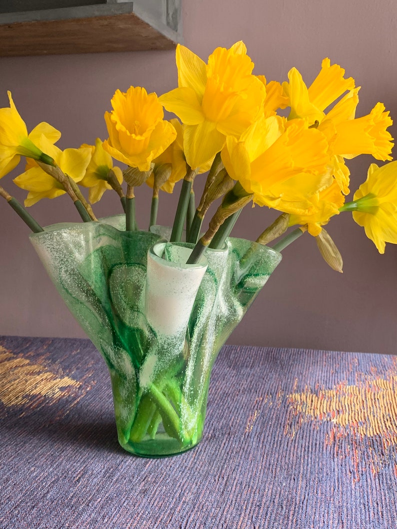 May include: A green glass vase with a ruffled, textured design holds a bouquet of yellow daffodils.