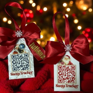 May include: Two Christmas tree decorations with red bows and ribbons. Each has a white tag featuring a QR code and a Santa Claus illustration. The text "Santa Tracker" is printed at the bottom of each tag.