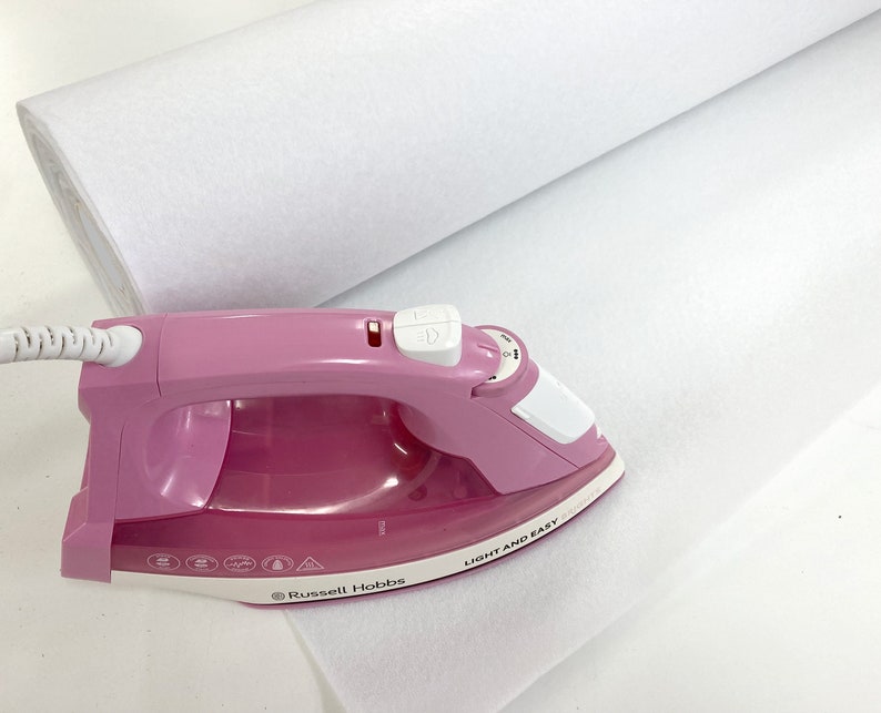 May include: A pink iron with a white handle and a white cord. The iron is on a white fabric roll. The iron has a button on the handle and a dial on the side. The iron has the text "LIGHT AND EASY" printed on the side. The iron also has the text "Russell Hobbs" printed on the side.