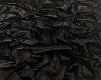 May include: A close-up shot of black fabric with a silky, shiny texture. The fabric is heavily draped, creating deep shadows and highlights that emphasize its flowing nature. The folds and creases give the material a luxurious appearance.