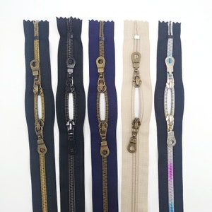 May include: Five different zipper pulls with metal sliders and teeth. The zippers are in black, navy blue, beige, silver, and pink.
