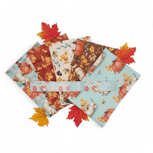 May include: A set of five fabric squares featuring an autumn theme with pumpkins, leaves, and acorns. The fabric squares are in shades of brown, orange, cream, and blue. The text "Autumn Awakening" is printed on a label.