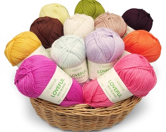 May include: A wicker basket filled with colorful yarn balls in shades of pink, purple, orange, yellow, brown, green, and cream. The yarn is labeled "LOVEFUL BIO BLEND". The basket is on a white background.