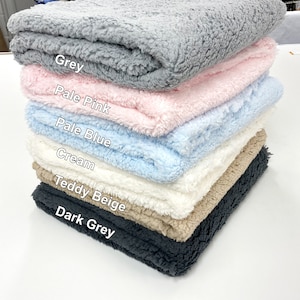 May include: A stack of six plush fabric swatches in various colours, including grey, pale pink, pale blue, cream, teddy beige, and dark grey. The swatches are arranged from lightest to darkest.