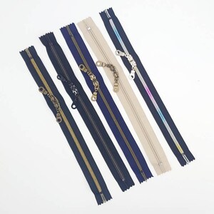 May include: Assortment of six zipper closures in various colors, including black, navy, gold, beige, and pink. Each zipper has a decorative metal pull.