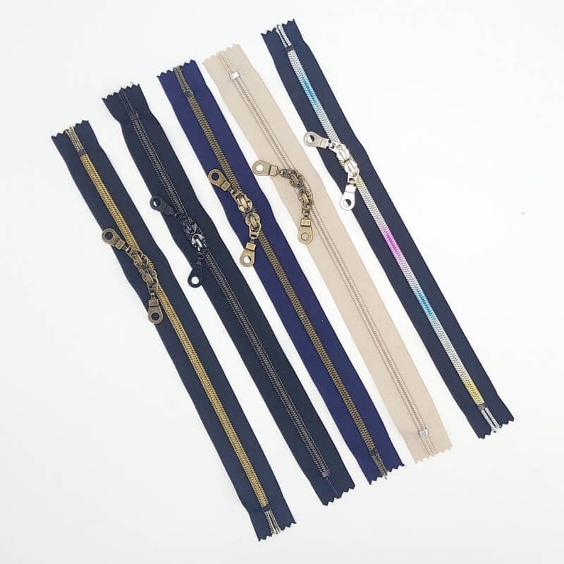 May include: Assortment of six zipper closures in various colors, including black, navy, gold, beige, and pink. Each zipper has a decorative metal pull.