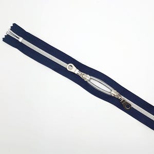 May include: A navy blue zipper with silver teeth and a silver slider. The zipper is open and the slider is in the middle of the zipper.