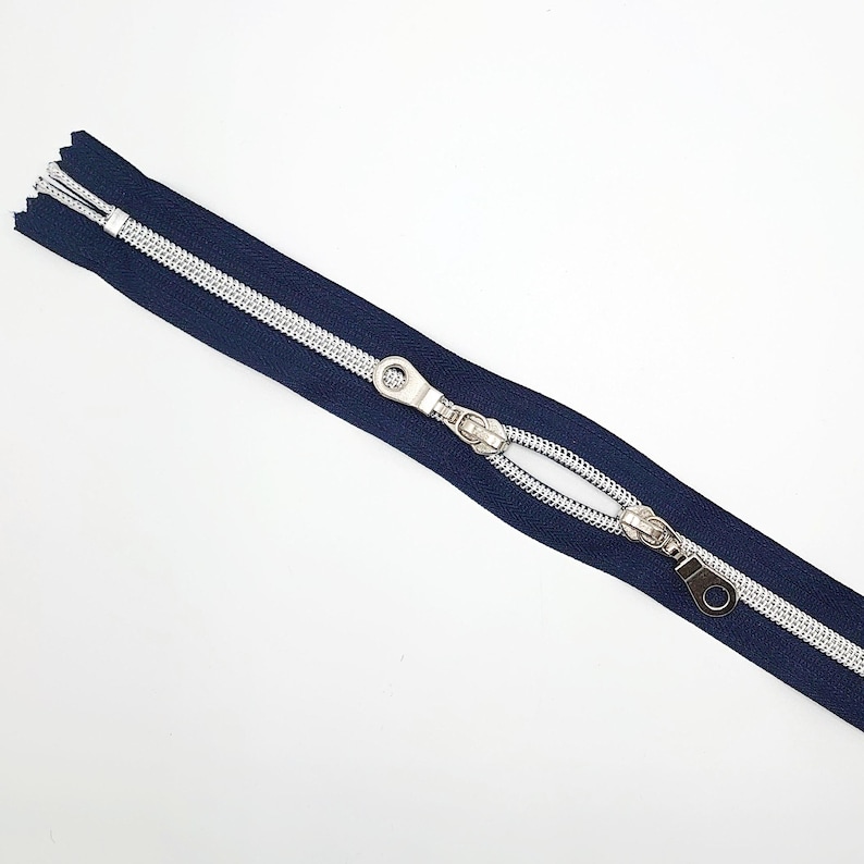 May include: A navy blue zipper with silver teeth and a silver slider. The zipper is open and the slider is in the middle of the zipper.
