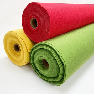 May include: Three rolls of felt fabric arranged together. One roll is bright red, one is a vibrant yellow, and the third is a light lime green. Each roll is wound around a central cardboard tube, showing the layered texture of the felt material.