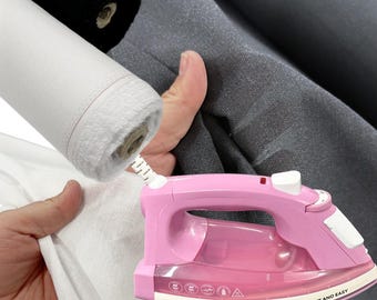 May include: A pink Russell Hobbs iron with the words "LIGHT AND EASY" printed on it. Rolls of white and black fabric are in the background, along with gray fabric. The iron is positioned near the fabric.