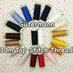 May include: A collection of 30m spools of Gutermann Top Stitch Thread in various colours, including red, blue, green, yellow, brown, black, and white. The spools are arranged in a circle on a white background with green polka dots.