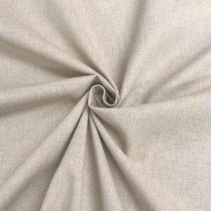 May include: Close-up of a beige fabric with a subtle texture. The fabric is folded and draped, showcasing its soft and smooth surface.