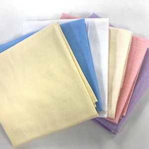 May include: An assortment of folded fabric squares in pastel shades: yellow, blue, white, cream, pink, and lavender. The fabric has a soft, smooth texture. The squares are arranged to display the range of colours. Each square is approximately 30 cm x 30 cm.