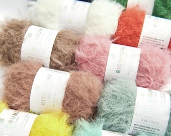 May include: A collection of fluffy yarn skeins in various colors, including white, brown, pink, and green. Each skein is labeled with the brand name and weight, 25g and 175m. The yarn has a soft, textured appearance.