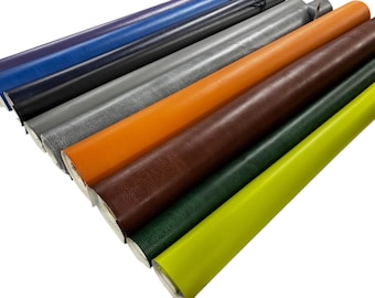 May include: An assortment of rolled leather hides in various colors, including blue, black, gray, orange, brown, green, and yellow. The hides are arranged diagonally, showcasing their textures and hues. The rolls are tightly wound, revealing the edges of the leather.