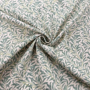 May include: A close-up of a white fabric with a repeating pattern of green willow branches. The fabric is folded and draped, showing the texture and detail of the design.