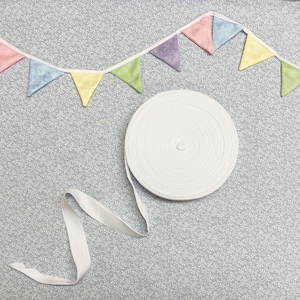 May include: A white cotton elastic band with a pastel coloured fabric bunting with triangle flags. The bunting is made of different shades of pink, purple, yellow and green.