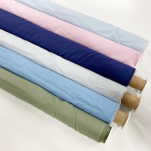 May include: Six rolls of fabric arranged diagonally, featuring solid colours including light blue, soft pink, navy blue, white, sky blue, and sage green. Each roll is wrapped around a cylindrical cardboard core, displaying a smooth texture.