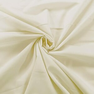 May include: A solid off-white fabric featuring a central swirl pattern that creates natural folds and drapes. The material has a smooth, matte texture and a consistent light cream color throughout, radiating outward from the center point.