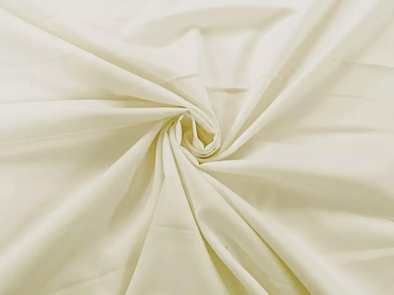 May include: A solid off-white fabric featuring a central swirl pattern that creates natural folds and drapes. The material has a smooth, matte texture and a consistent light cream color throughout, radiating outward from the center point.