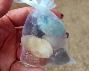 May include: A white organza bag filled with various tumbled stones, including a light blue, a white, a dark grey, and a light brown stone.