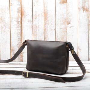 Peut inclure: Un sac &agrave; bandouli&egrave;re en cuir marron avec une longue sangle r&eacute;glable. Le sac a une fermeture &agrave; glissi&egrave;re et un rabat avec une boucle en m&eacute;tal.