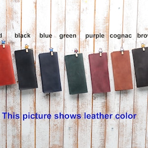 May include: Eight leather swatches hanging from clothes pegs on a white wood background. The swatches are labelled with the colours: red, black, blue, green, purple, cognac, and brown.