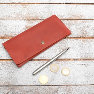 May include: A red leather wallet with a silver pen and three gold coins on a white wooden surface.