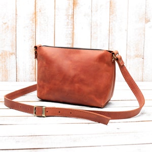 Peut inclure: Un sac &agrave; bandouli&egrave;re en cuir marron avec une longue sangle r&eacute;glable. Le sac a un design simple et est fait de cuir de haute qualit&eacute;.