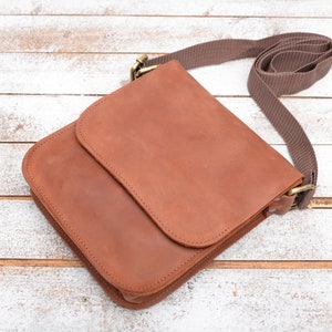 May include: A brown leather crossbody bag with a flap closure and a brown adjustable strap.